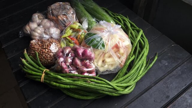 Assorted fresh groceries from the traditional market featuring long beans garlic shallots and mixed vegetables placed together on a dark wooden surface