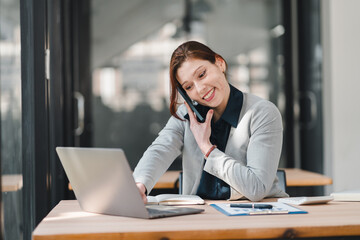 Fototapeta premium A business woman having a phone conversation while working on a laptop in an office
