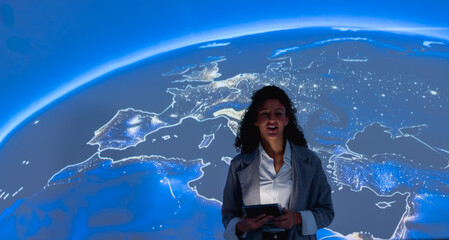 Woman stands before glowing global map. She holds tablet, smiles warmly. Earth's illuminated continents shine beneath her. Modern, tech-focused presentation setting. © Father_Studio