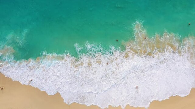 Aerial top down view of big ocean waves crashing on a sandy beach. Nature background with sea surf foam for summer vacation and travel concepts.
