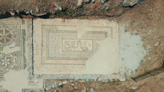 Aerial top-down drone shot pulling up from a beautifully preserved ancient Roman mosaic floor to reveal the surrounding archaeological excavation site and ruins.