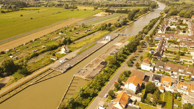 Aerial view of the canal lock in Saint-Omer, featuring concrete structures, adjacent residential housing, and surrounding agricultural fields in Saint-Omer, Hauts-de-France, France.