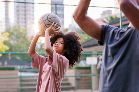 Girl prepares to shoot basketball, defender raises arms.