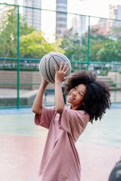 Girl smiles, ready to shoot a basketball outdoors.
