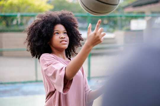 Girl with curly hair spins basketball on finger outdoors.
