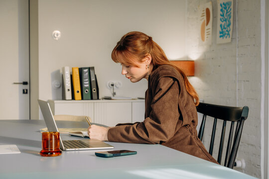 A woman using a laptop and writing in a notebook in the office