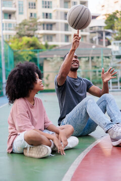 Friends relax on a basketball court, one spins ball.