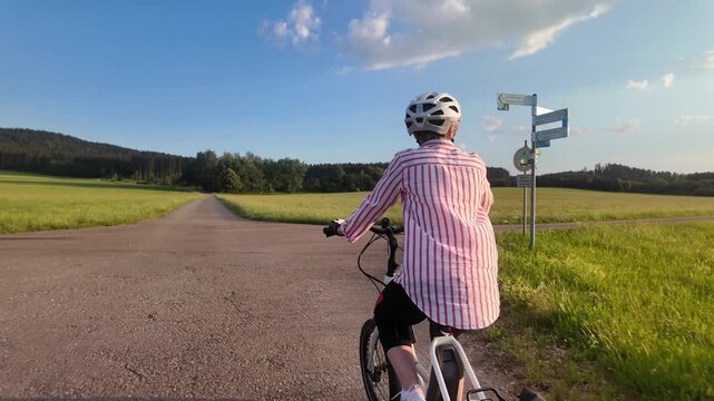 Middle aged woman riding electric bicycle on paved path through green fields