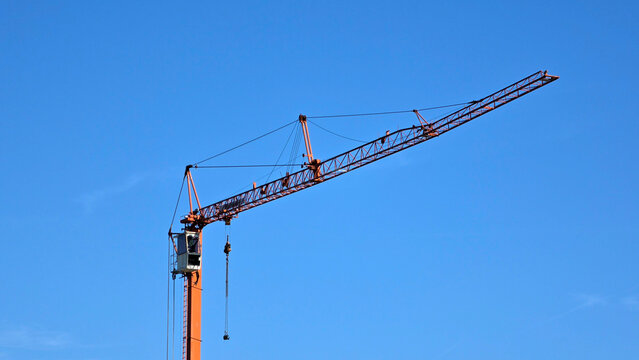 Orange industrial tower crane with extended horizontal jib against a solid blue sky