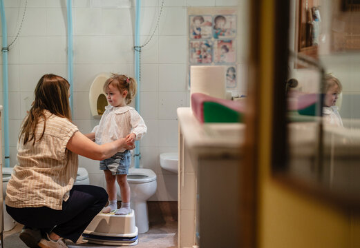 Mother assisting child with potty training in school toilet
