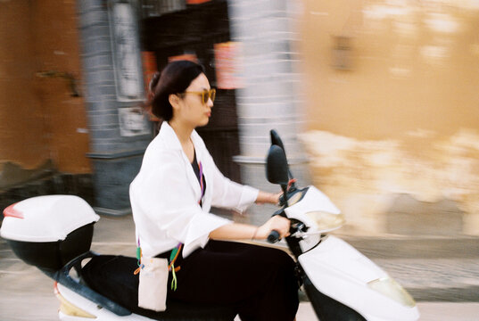 Young Woman Riding Scooter Through a Village Street on a Sunny Day