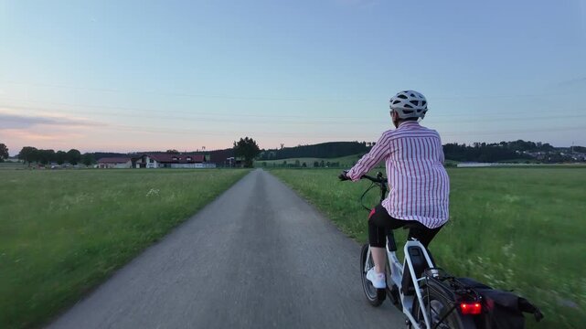 Middle aged woman riding electric bicycle on paved path through green fields