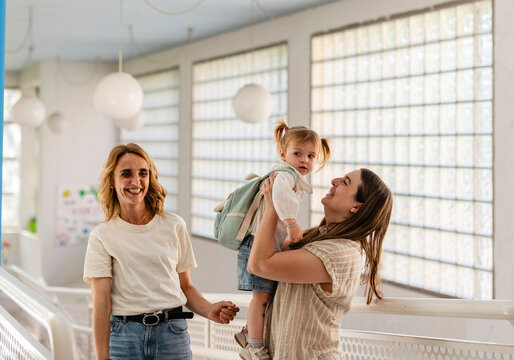 Two mothers dropping off happy toddler at preschool