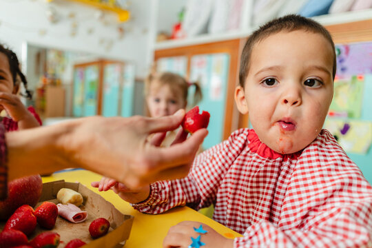 Child receiving a strawberry during snack time in kindergarten