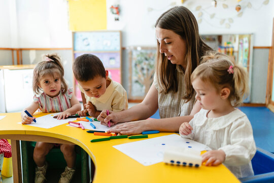 Teacher helping toddlers drawing and coloring in classroom
