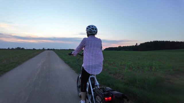 Middle aged woman riding electric bicycle on paved path through green fields
