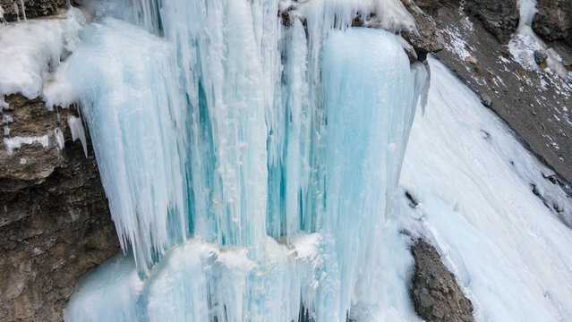 Aerial view of a frozen waterfall with vibrant blue icicles clinging to a rugged rocky cliff face in Khunjerab National Park, Gilgit, Pakistan.