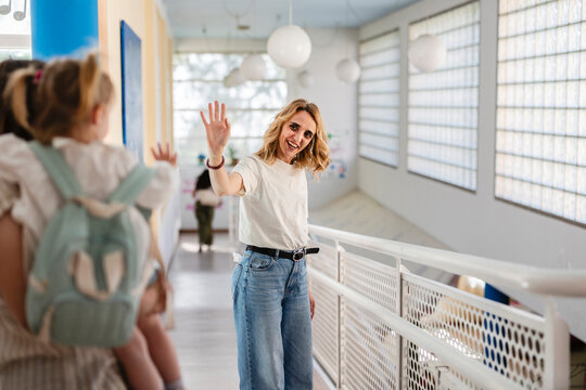 Happy teacher or caregiver waving goodbye to little girl