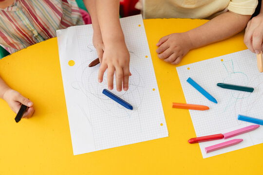 Children hands drawing coloring with crayons on yellow table