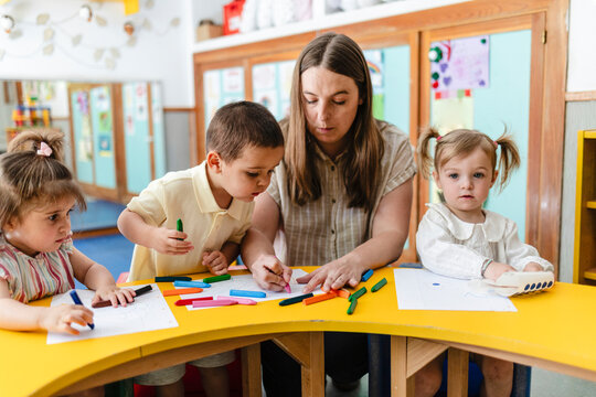 Teacher guiding young children drawing and learning in nursery