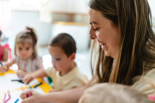 Teacher smiling watching young children learning and drawing