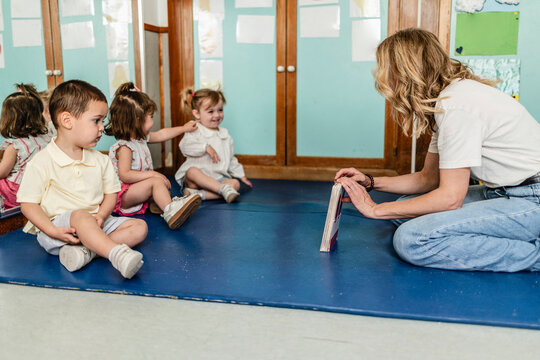 Teacher reading book to small children in kindergarten
