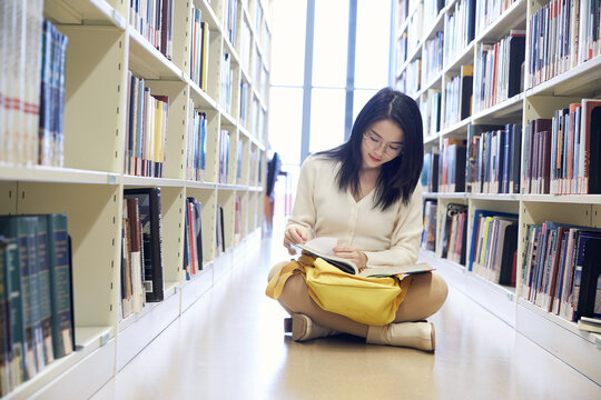 Young female student reading in library aisle