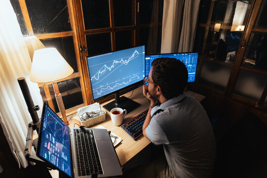 Man trading and Analyzing Stock Charts on Multiple Screens at Night