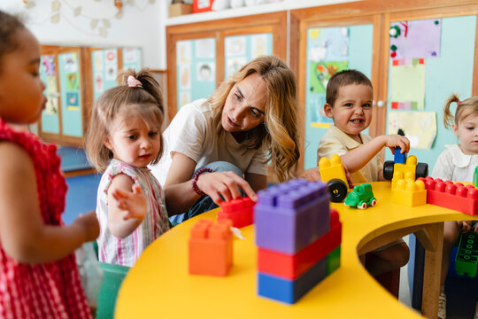 Teacher helping multiracial children building blocks in kindergarten