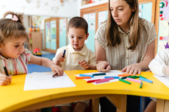 Preschool teacher supervising children drawing with crayons