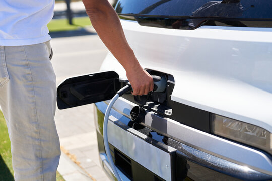 Person plugging electric car charging cable, sustainable