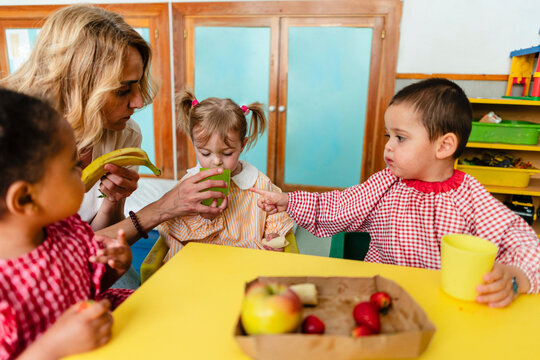 Teacher helping multiracial children eating healthy snack at school