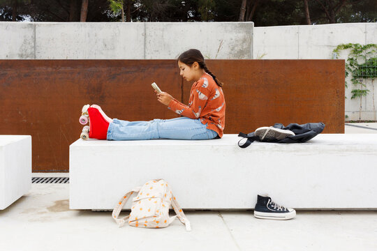 Girl Uses Phone While Sitting on a Bench 