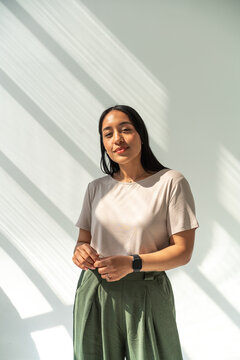 Confident Brunette Woman Standing in Sunlit Studio Wearing Casual Top