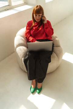 Redhead Woman Working on Laptop and Making a Call In Minimal Studio