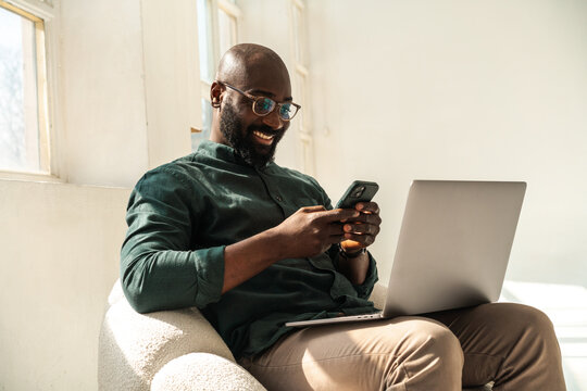 Smiling Man with Glasses Working Remotely With Laptop and Phone
