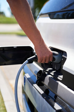 Person plugging electric vehicle charging cable into EV car