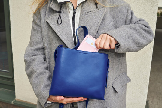 Woman places pink wallet with card in blue bag 