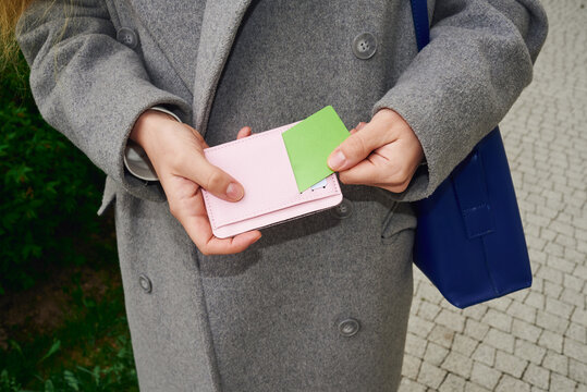 Woman holds wallet and green credit card while standing outdoors