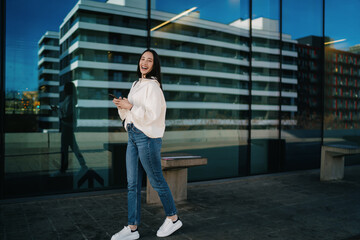 Naklejka premium Young lady wearing earbuds and holding mobile phone while waiting for commute, listening to audio book or podcast, urban travel, serenity, mindfulness, contemporary digital lifestyle, city.