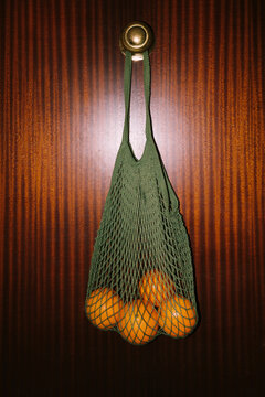 Mesh bag hangs on a door knob with oranges inside