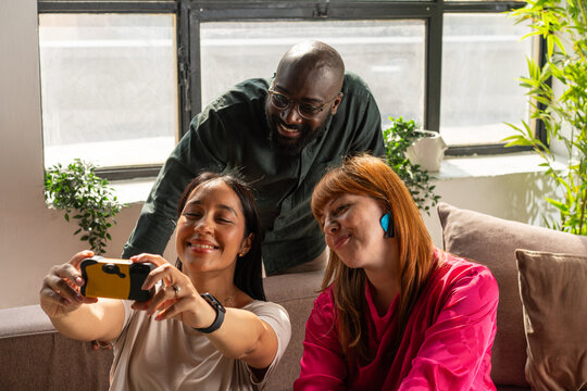 Three Friends Taking A Selfie On A Cozy Couch In A Bright Office