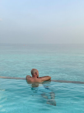 Man relaxing in a pool villa in the Maldives with ocean behind