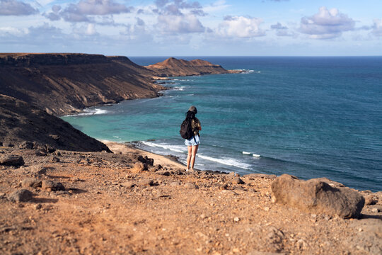 Woman standing on cliff overlooking dramatic coastline at sunset on Sal Island, Cape Verde