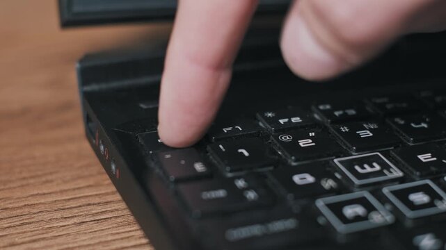 Side angle view of a male finger repeatedly tapping the black ESC key on a laptop keyboard. The urgent action suggests frustration, aborting a process, or a software error.