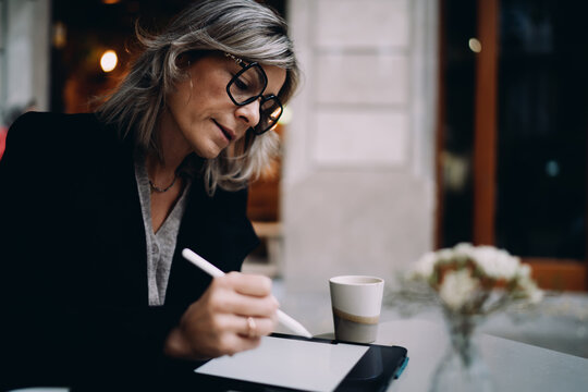 Concentrated woman using stylus pen to sign digital document on tablet at cafe table, online banking and secure payment transaction, mature professional working with financial software