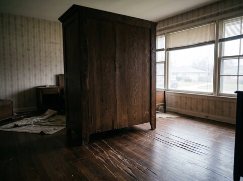 Back view vintage wooden armoire sliding across hardwood floor toward window earthquake