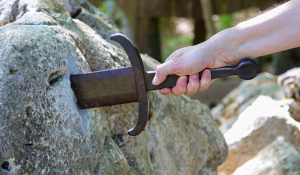Hand of a man trying to pull the legendary Excalibur sword from a rock