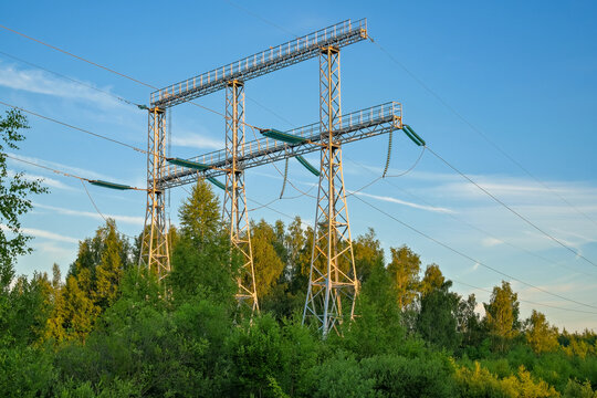 Metal electrical transmission portal with suspension insulators and overhead cables near woodland