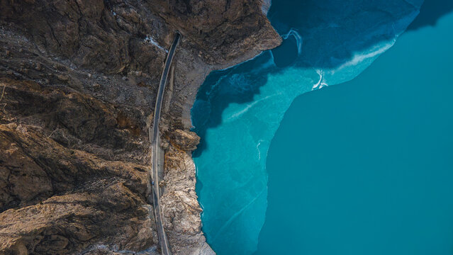 Aerial view of the turquoise waters of Attabad Lake with a road winding along the rocky cliffs in Hunza Nagar, Gilgit, Pakistan.